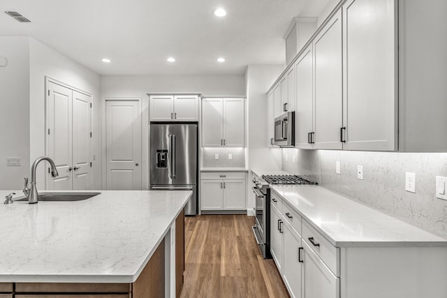 kitchen with white cabinetry, stainless steel appliances, light stone countertops, hardwood / wood-style flooring, and sink