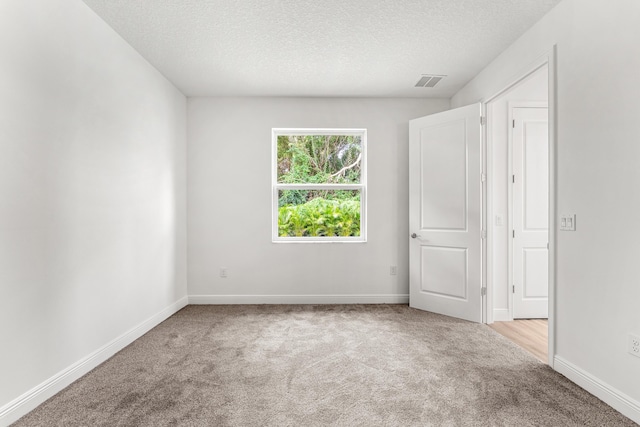 spare room featuring a textured ceiling and light colored carpet