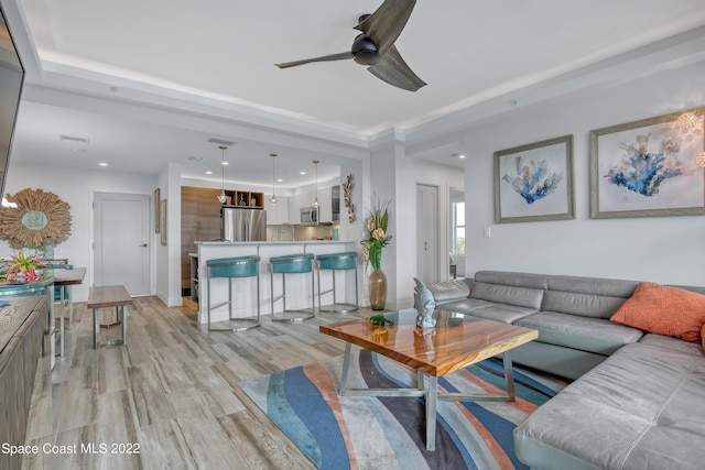 living room with a tray ceiling, recessed lighting, a ceiling fan, and light wood finished floors