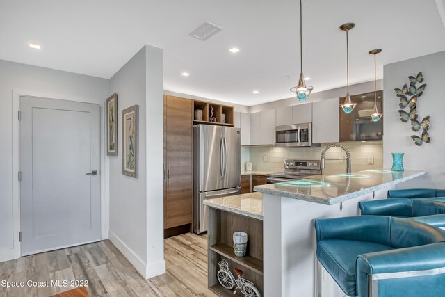 kitchen with appliances with stainless steel finishes, tasteful backsplash, a breakfast bar, kitchen peninsula, and light hardwood / wood-style floors