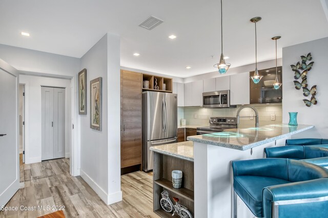 kitchen featuring appliances with stainless steel finishes, tasteful backsplash, light wood-type flooring, light stone countertops, and a kitchen breakfast bar