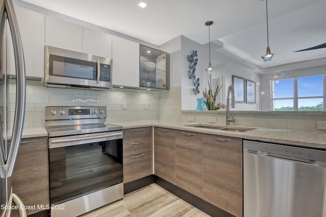 kitchen featuring stainless steel appliances, white cabinets, sink, decorative backsplash, and light stone countertops