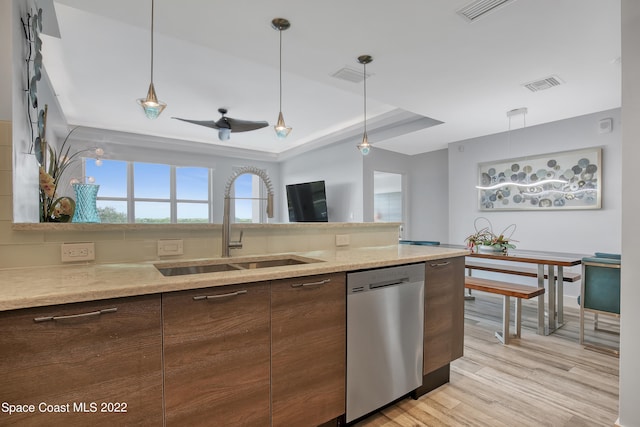 kitchen with dishwasher, light wood-type flooring, a tray ceiling, and decorative light fixtures