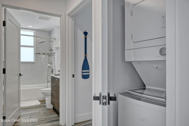 laundry area featuring stacked washer and clothes dryer and light wood-type flooring