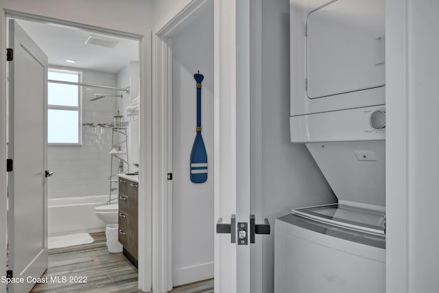 laundry area featuring light wood-type flooring, visible vents, stacked washing maching and dryer, and laundry area