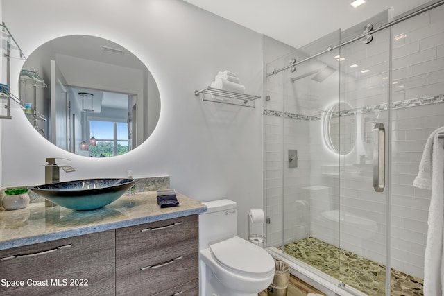 bathroom featuring a shower with door, vanity, and toilet