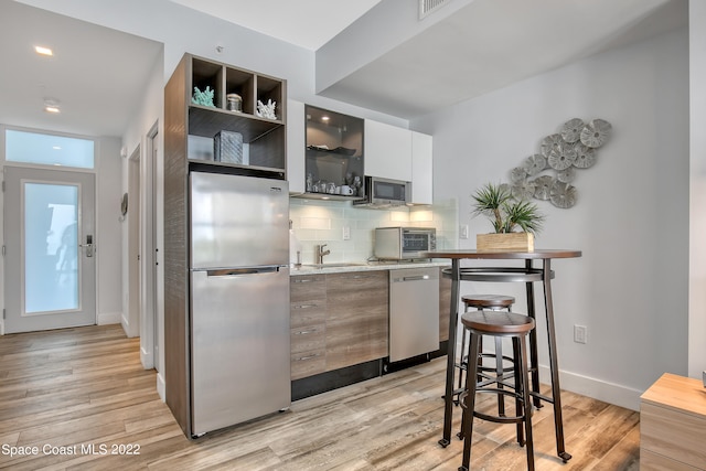 kitchen featuring a breakfast bar area, tasteful backsplash, white cabinets, stainless steel appliances, and light hardwood / wood-style floors