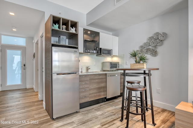 kitchen with light countertops, tasteful backsplash, appliances with stainless steel finishes, and light wood-style floors