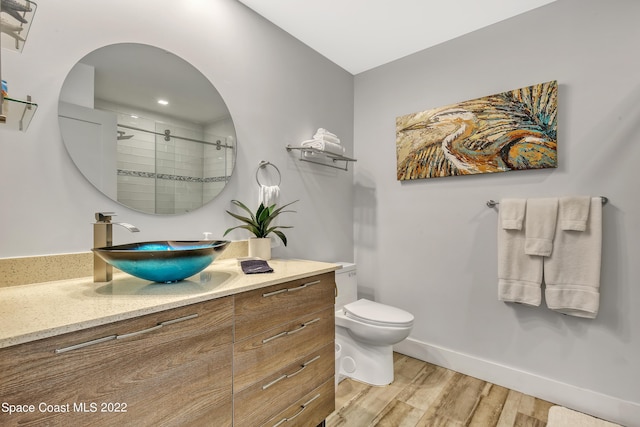bathroom with vanity, toilet, baseboards, a shower stall, and wood finished floors