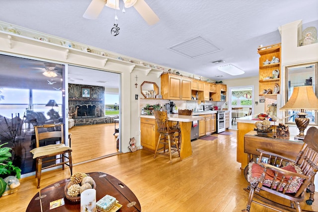 living room featuring a textured ceiling, a fireplace, ceiling fan, and light wood-type flooring