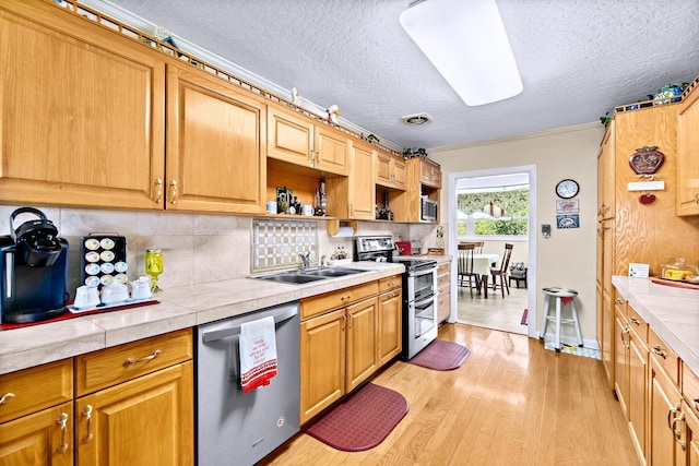 kitchen with appliances with stainless steel finishes, sink, backsplash, tile counters, and light hardwood / wood-style flooring