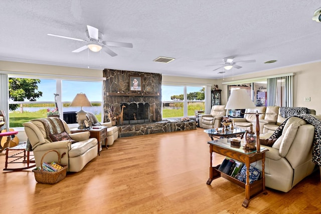 living room with a stone fireplace, light hardwood / wood-style flooring, a textured ceiling, and ceiling fan