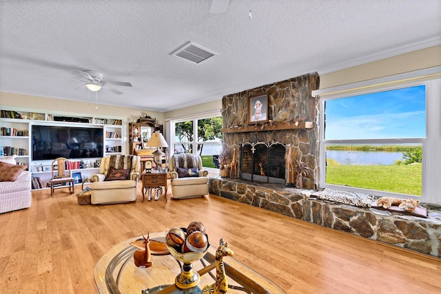 living room featuring a stone fireplace, wood-type flooring, ceiling fan, a water view, and a textured ceiling