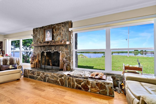 living room featuring crown molding, a water view, wood-type flooring, a textured ceiling, and a stone fireplace