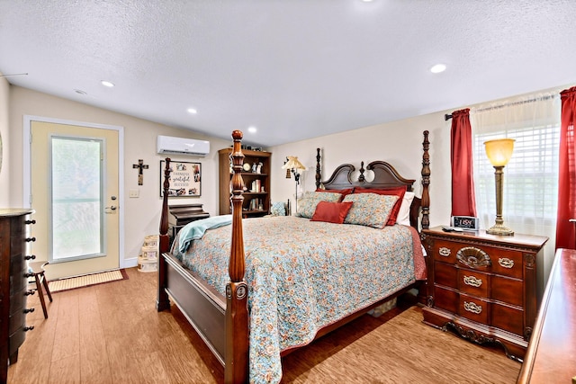 bedroom with lofted ceiling, a wall unit AC, a textured ceiling, and light wood-type flooring