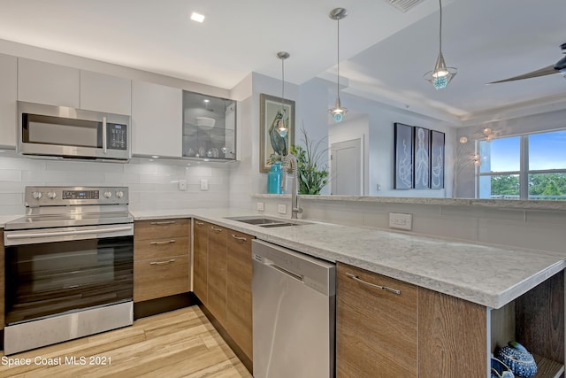 kitchen featuring a sink, a peninsula, modern cabinets, stainless steel appliances, and decorative backsplash