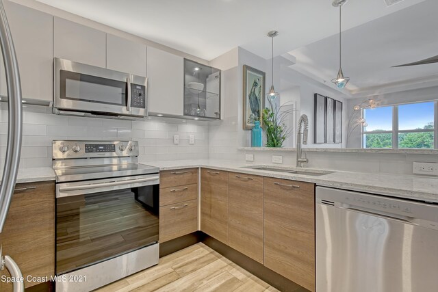 kitchen with a sink, light stone countertops, modern cabinets, stainless steel appliances, and decorative backsplash
