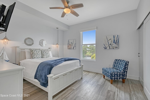 bedroom featuring a ceiling fan, a closet, baseboards, and light wood finished floors
