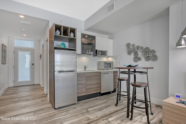 kitchen with light hardwood / wood-style flooring, tasteful backsplash, white cabinets, appliances with stainless steel finishes, and sink