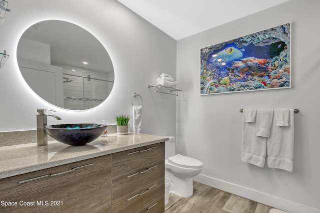 full bathroom featuring baseboards, wood finished floors, toilet, vanity, and a stall shower