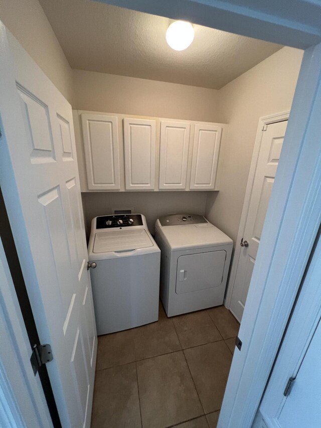 clothes washing area with washing machine and dryer, cabinets, a textured ceiling, and light tile patterned flooring