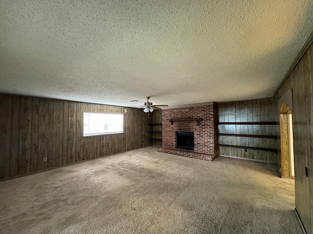 unfurnished living room with wooden walls, brick wall, light carpet, a textured ceiling, and a brick fireplace