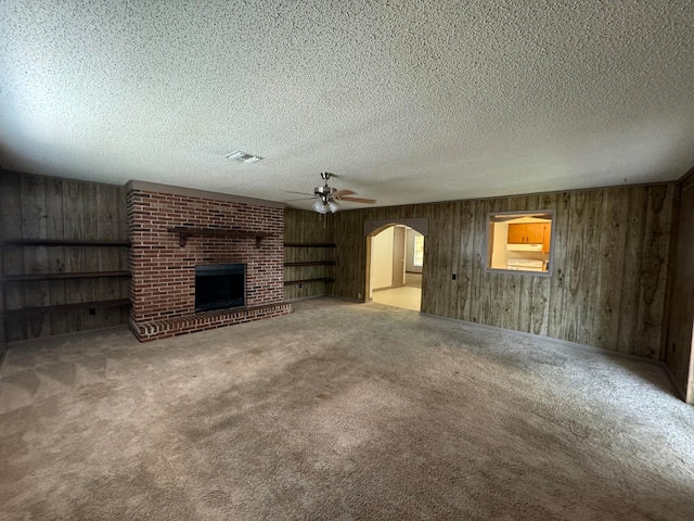 unfurnished living room with light carpet, wooden walls, a brick fireplace, and a textured ceiling