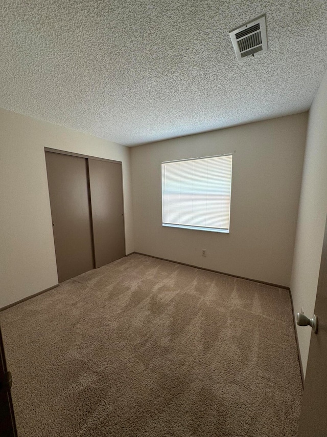 unfurnished bedroom with light carpet, a closet, and a textured ceiling