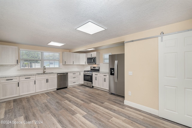 kitchen with a barn door, sink, stainless steel appliances, and light hardwood / wood-style flooring