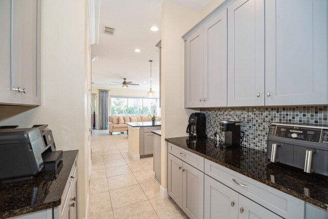 kitchen featuring dark stone counters, tasteful backsplash, light tile patterned floors, and ceiling fan