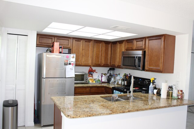 kitchen with light tile patterned flooring, kitchen peninsula, light stone counters, electric stove, and white refrigerator