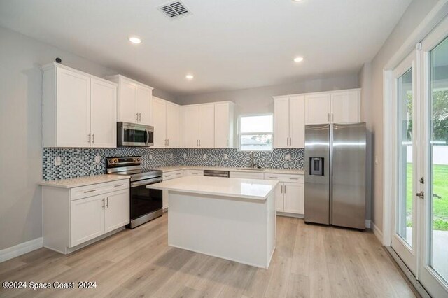 kitchen with a kitchen island, tasteful backsplash, stainless steel appliances, white cabinetry, and light wood-type flooring