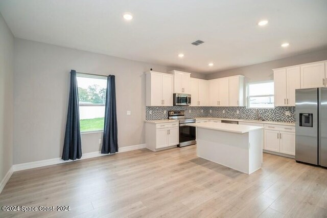 kitchen featuring a kitchen island, light hardwood / wood-style flooring, stainless steel appliances, decorative backsplash, and white cabinets