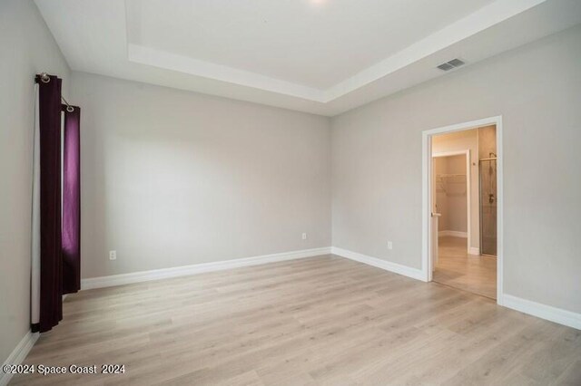 spare room featuring a tray ceiling and light hardwood / wood-style flooring