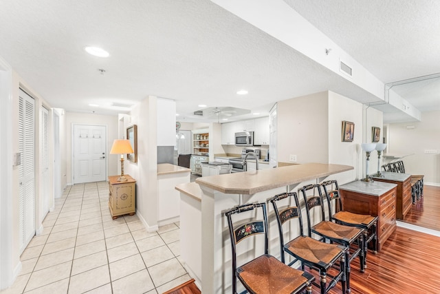 kitchen featuring a textured ceiling, a kitchen breakfast bar, kitchen peninsula, stainless steel appliances, and white cabinets