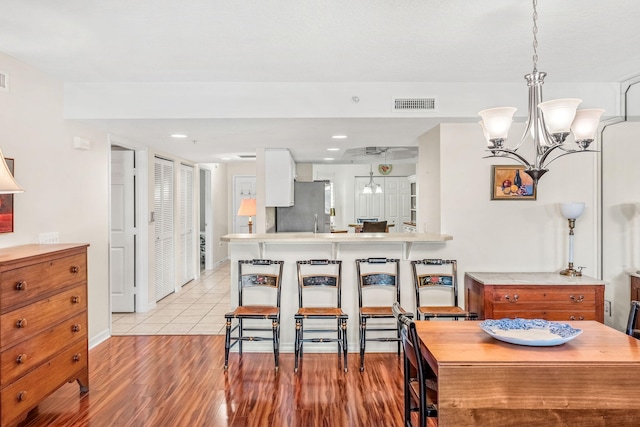 kitchen featuring a chandelier, light wood-type flooring, stainless steel refrigerator, kitchen peninsula, and pendant lighting