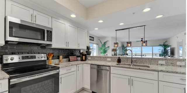 kitchen with appliances with stainless steel finishes, light stone countertops, sink, white cabinetry, and kitchen peninsula