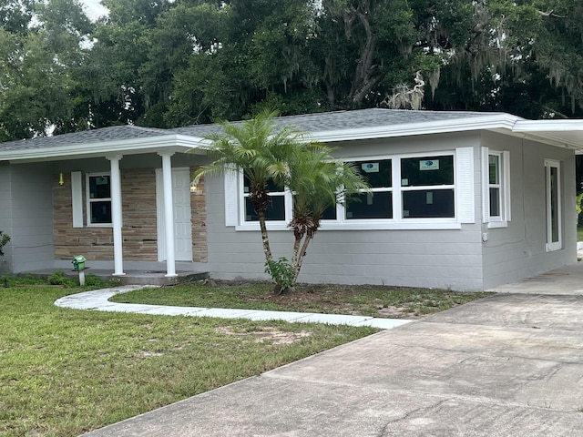 view of front of house featuring a shingled roof, a front yard, covered porch, and concrete driveway