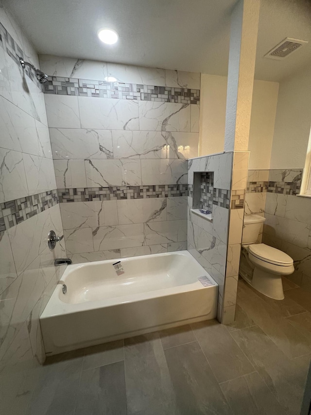 bathroom with toilet, tiled shower / bath combo, and tile walls