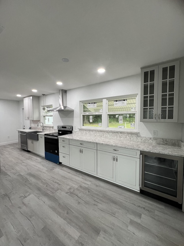 kitchen with beverage cooler, appliances with stainless steel finishes, wall chimney range hood, light stone countertops, and glass insert cabinets