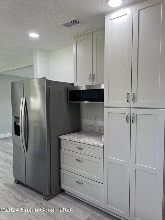 kitchen featuring light hardwood / wood-style flooring, light stone countertops, a textured ceiling, and appliances with stainless steel finishes