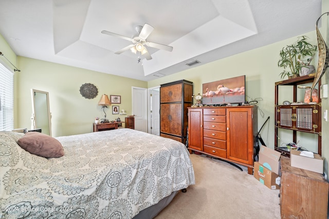 bedroom with ceiling fan, light carpet, and a tray ceiling