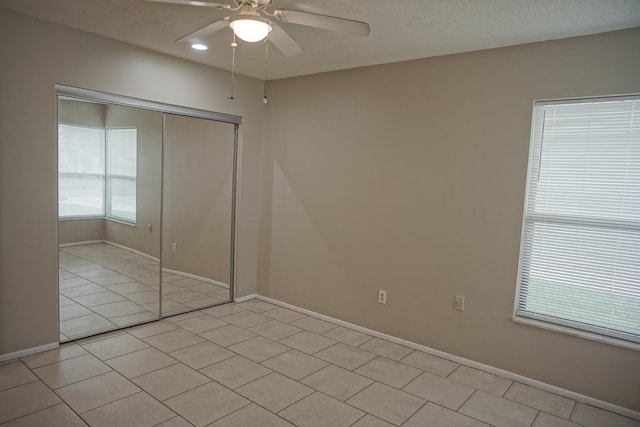 unfurnished bedroom with ceiling fan, a closet, multiple windows, and light tile patterned flooring