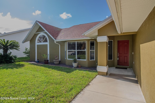 property entrance with a shingled roof, a lawn, and stucco siding