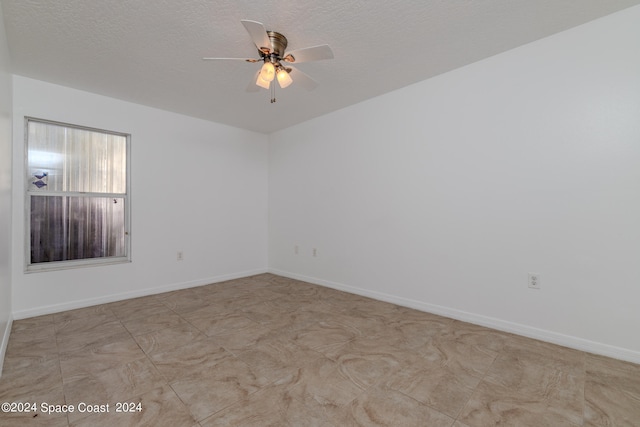 spare room featuring ceiling fan, light tile patterned floors, and a textured ceiling