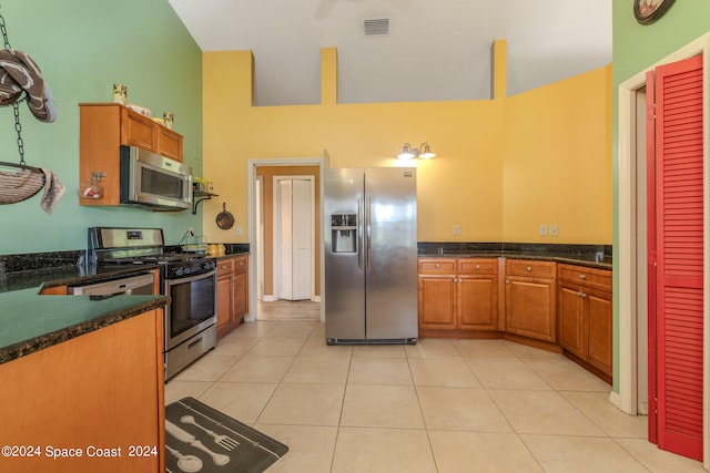 kitchen featuring light tile patterned floors, stainless steel appliances, dark stone counters, and a towering ceiling