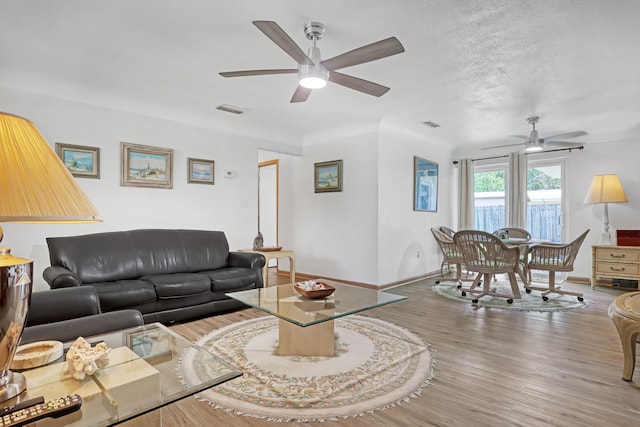 living room featuring wood-type flooring, a textured ceiling, and ceiling fan