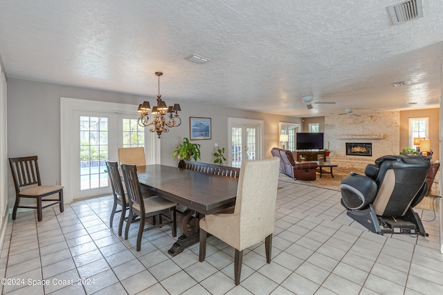 dining area with french doors, a fireplace, light tile patterned flooring, a textured ceiling, and ceiling fan with notable chandelier