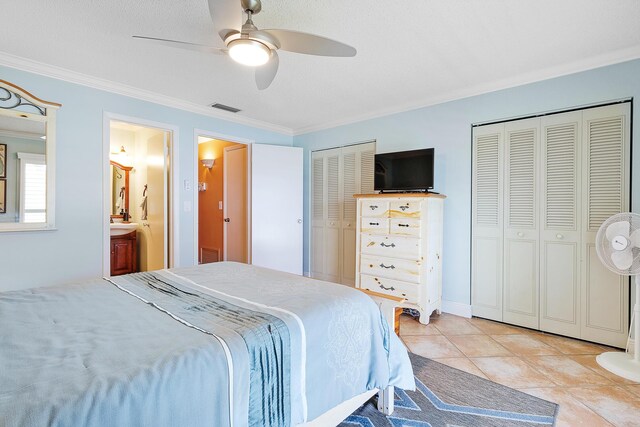 bedroom with crown molding, ensuite bath, light tile patterned floors, multiple closets, and ceiling fan