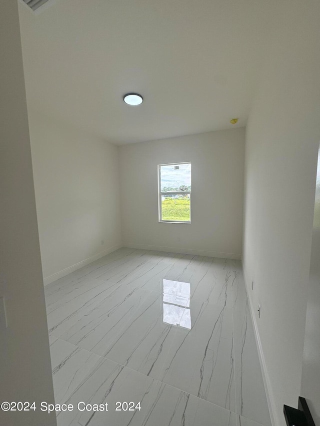 spare room featuring marble finish floor and baseboards